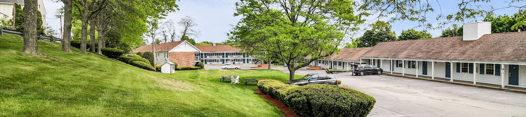 A sunny, well-kept college campus or motel exterior with green lawns, trees, and low-rise buildings lining a driveway. Top it.