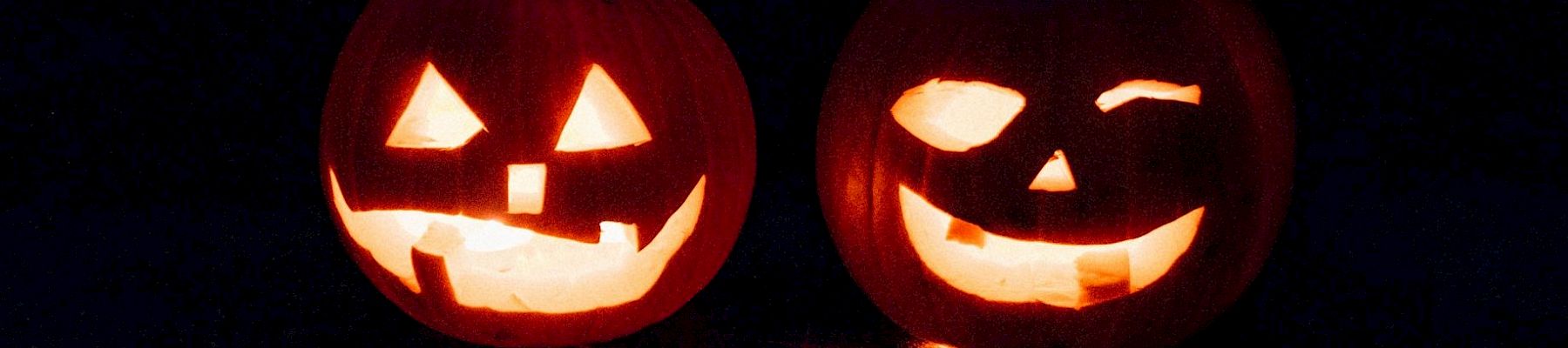 Two lit Jack-o'-lanterns glowing from carved faces in the dark, sharing a spooky Halloween vibe.