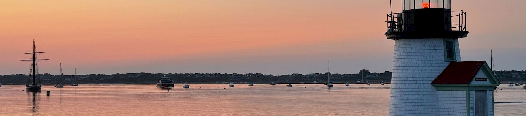 A serene sunset over a calm bay with a small white lighthouse, a lone fisherman on the shore, and gentle colors reflecting on the water.