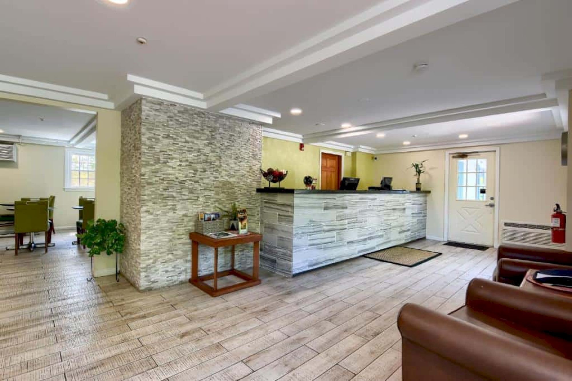 A modern hotel lobby with a stone-front desk, a small table, potted plants, tiled floor, and seating area, warmly lit and welcoming.
