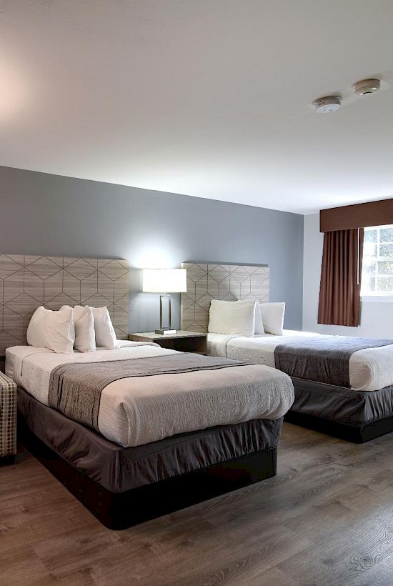 A hotel room with two beds, a plaid sofa, nightstands, lamps, a framed picture, and large windows with curtains.