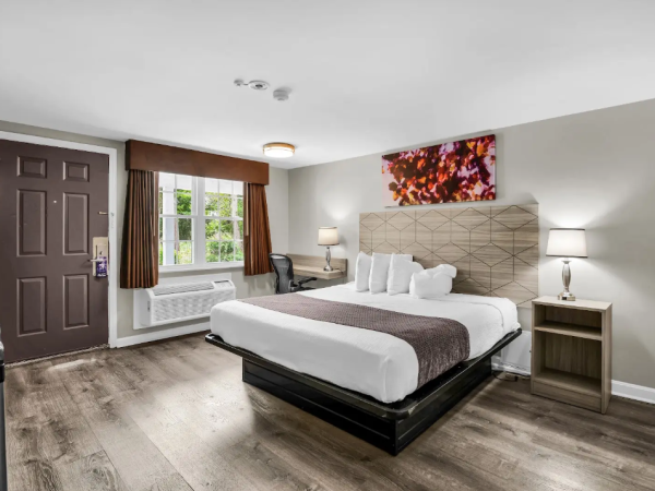 A modern bedroom with a bed, nightstands, lamps, window with curtains, and a framed wall art painting.