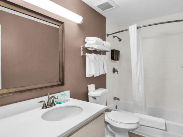 Tidy bathroom with vanity sink, toilet, bathtub, and neatly folded white towels near the shower.