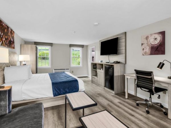 A modern hotel room with two beds, a work desk and chair, a wall-mounted TV, a small lounge area, and a window view, bright and stylish.