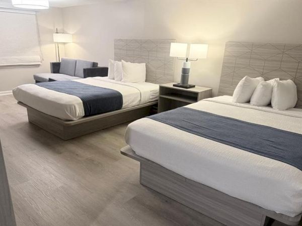 A hotel room with two queen beds, matching nightstand lamps, and a clean, modern gray-blue color scheme.