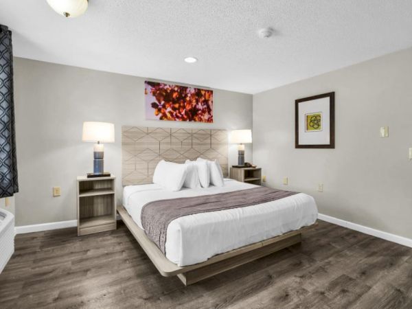 A modern hotel bedroom with a large bed, two matching nightstands, lamps, a framed art piece, and neutral tones on the walls and floor, bright and tidy.