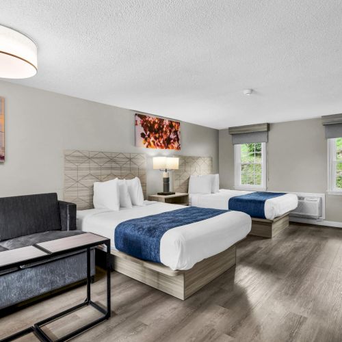 A modern hotel-style room with two beds, a seating area, and a small desk, in a bright, clean space.