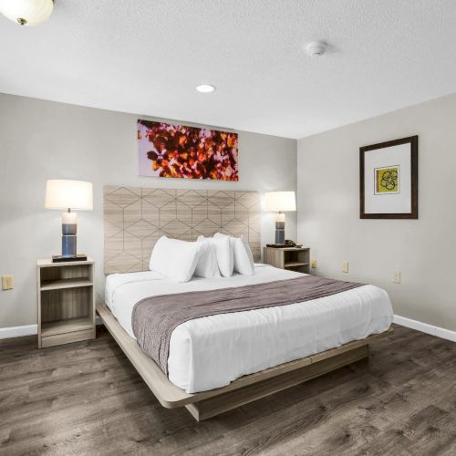 A modern bedroom with a large bed, two bedside lamps, framed art, and neutral walls and curtains.