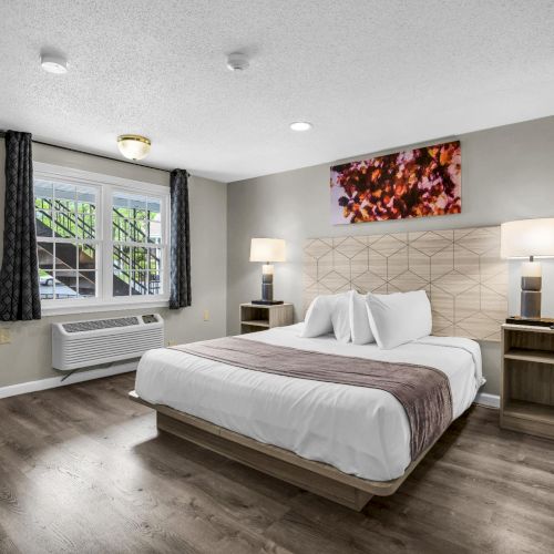 A modern bedroom with a bed, lamps, framed art, curtains, window A/C, and tiled accent wall.