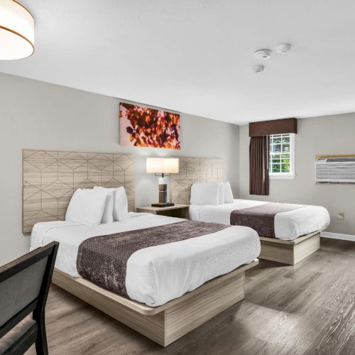 A modern hotel-style bedroom with two beds, lamps, windows with blinds, and a wall art painting.