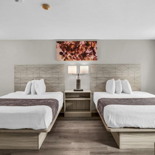 A modern twin bedroom with two made-up beds, geometric headboards, a bedside lamp, wall art, and a sunny window.