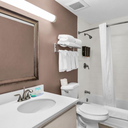 A clean bathroom with a sink and mirror, toilet, towels on a rack, and a shower with a white curtain.