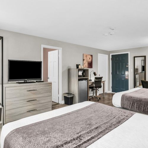 A modern hotel room with two beds, TV stand, desk, and large window with curtains.