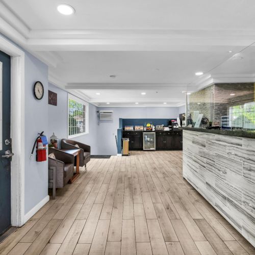 Bright lobby with windows and door, a marble front desk, and a mirrored counter with snacks behind it.
