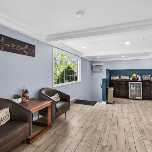 A bright lounge with brown leather seating and a small table, plus a counter coffee setup along the wall.