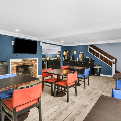 A bright restaurant with blue walls, booth seating, tables, a bar counter, a brick fireplace, and wall TV screens.