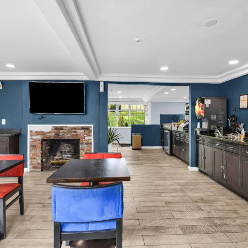 A modern caf&eacute; kitchen area with dark counters, espresso machines, tables, TVs, and a brick fireplace in the dining room.