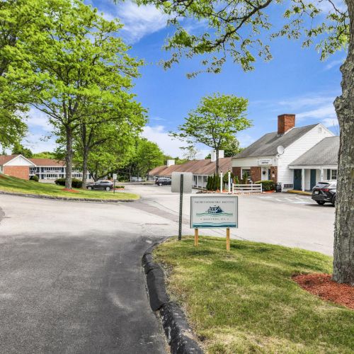 A hotel driveway with the &ldquo;Northshore Hotel&rdquo; sign, white buildings, parked cars, and green trees under a blue sky.
