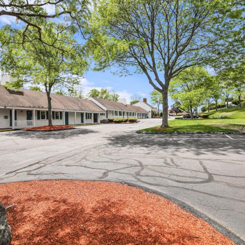A quiet motel-like row of white buildings along a driveway, surrounded by lush green trees and lawns.