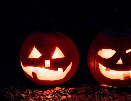 Two lit Jack-o'-lanterns glowing from carved faces in the dark, sharing a spooky Halloween vibe.