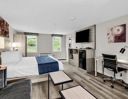 A modern hotel room with a bed, desk, office chair, wall art, and a mounted TV.